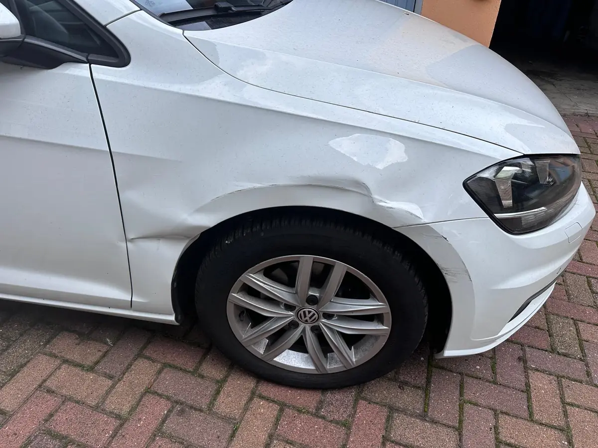 Weißer VW mit Delle im vorderen Kotflügel und Kratzern am Radlauf
