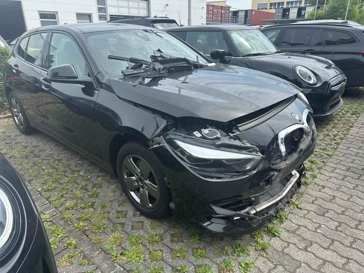 Schwarzer BMW 1er mit schwerem Frontschaden: Motorhaube aufgebogen, Scheinwerfer und Stoßfänger zerstört