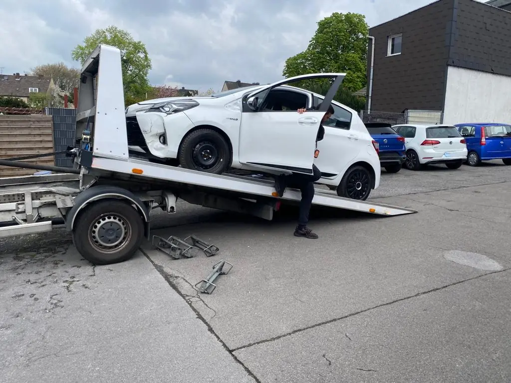 Weißer Toyota Yaris mit Frontschaden wird auf unseren Abschleppwagen gefahren