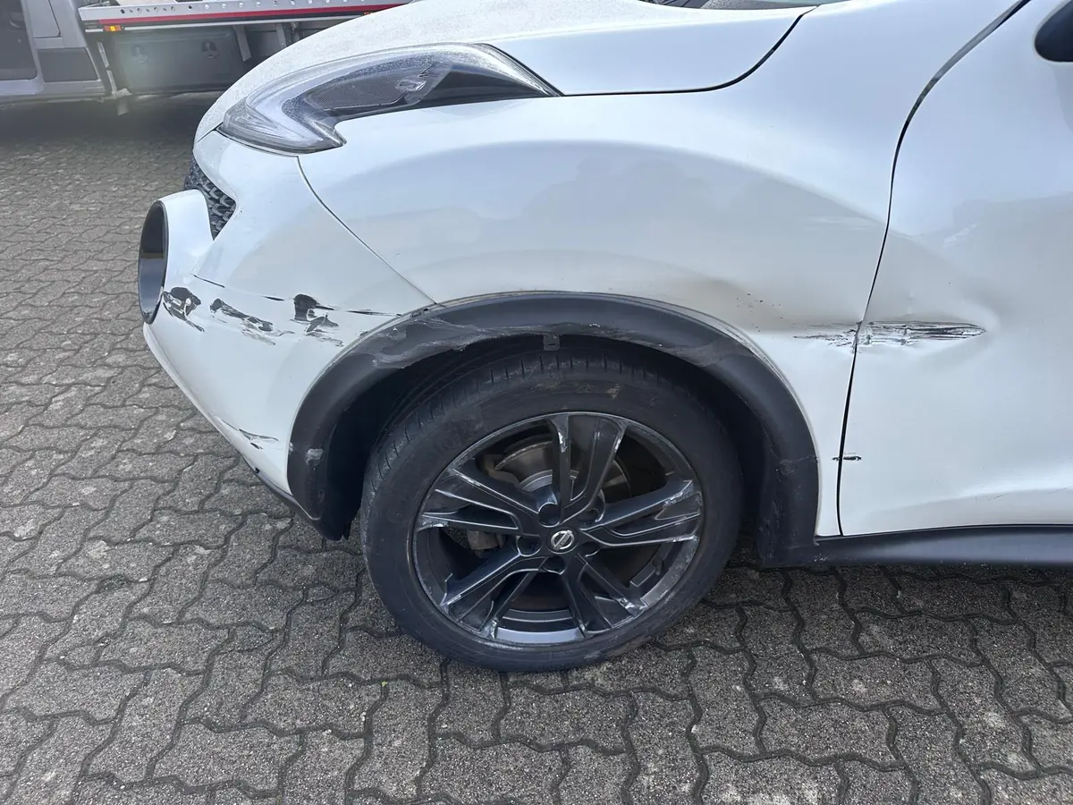 Weißer Nissan Juke mit Schrammen an Stoßfänger, Radlauf, Kotflügel und Tür vorne links