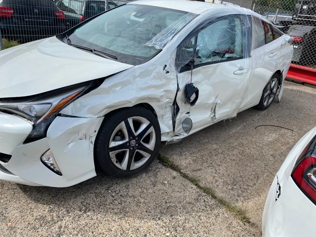 Weißer Toyota Prius mit schwerem Seitenschaden: Tür eingedrückt, Außenspiegel hängt lose, Kotflügel vorne beschädigt