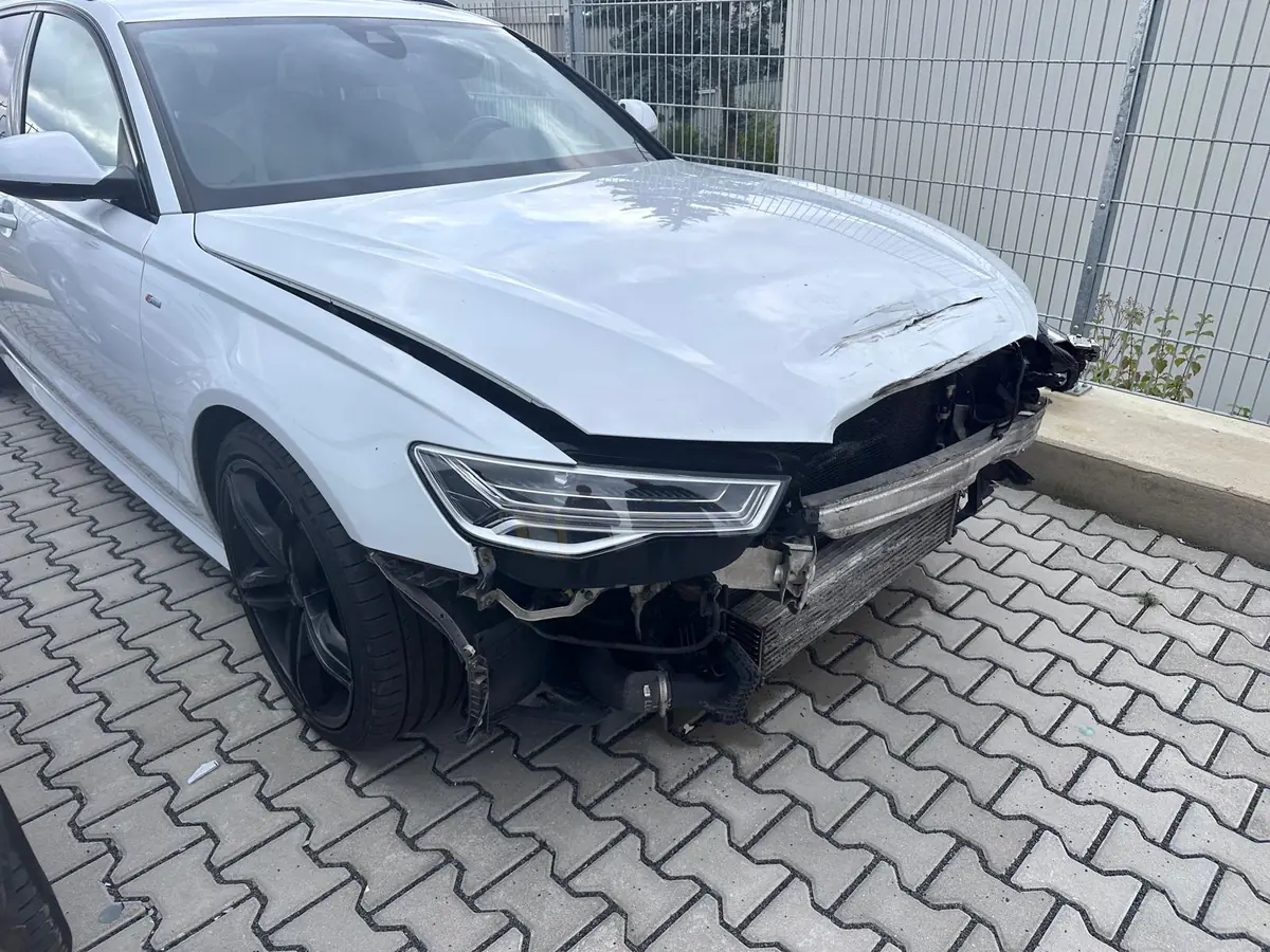 Weißer Audi A6 Avant mit schwerem Frontschaden: Motorhaube eingedrückt, Stoßfänger abgerissen, Kühler und Scheinwerfer frei liegend